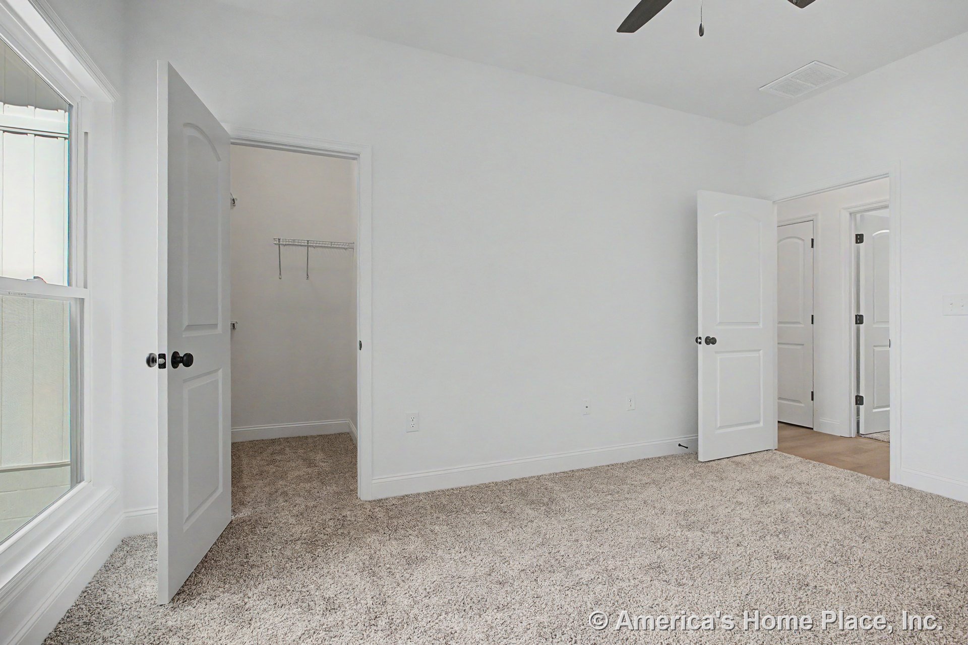 Carpeted bedroom with neutral walls, white baseboards and trim, large window, ceiling fan, paneled doors, and walk-in closet featuring wire shelving.