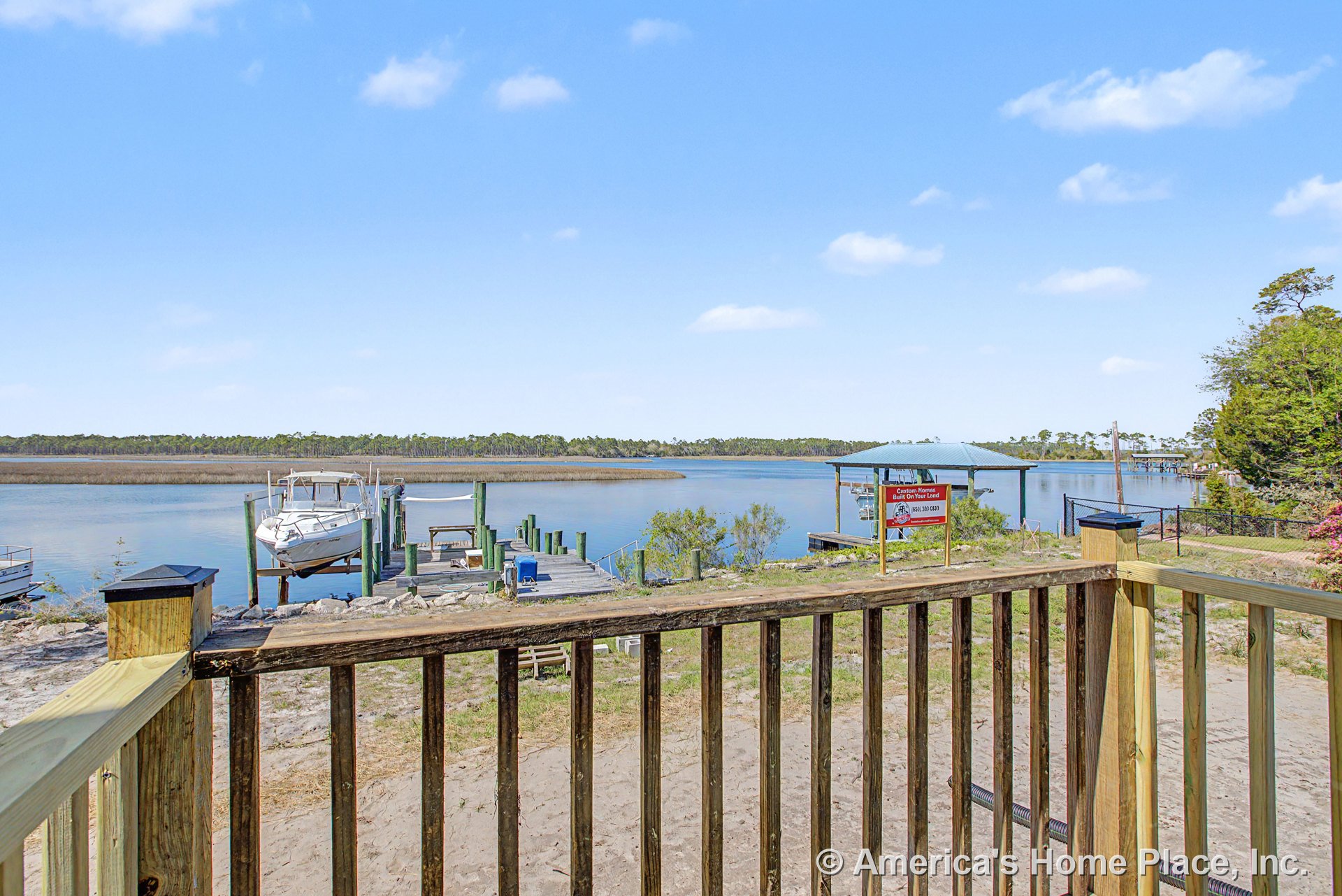 Wood deck with sturdy railing facing a private dock and waterfront, featuring a covered boat slip, exterior fencing, and pier structure.