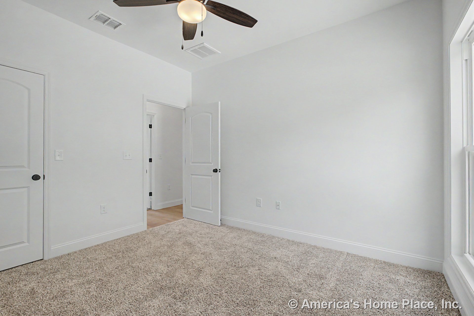 Bedroom with light carpet flooring, white walls, white trim and baseboards, ceiling fan with light fixture, double panel doors, and large window allowing natural light.