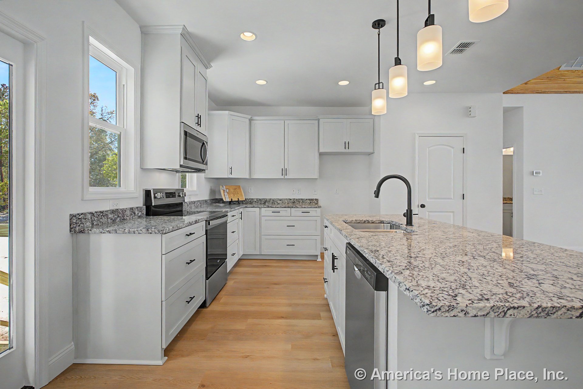 White shaker cabinets and granite countertops with stainless steel appliances, pendant lights above a spacious island, light wood flooring, double windows, recessed lighting, and
