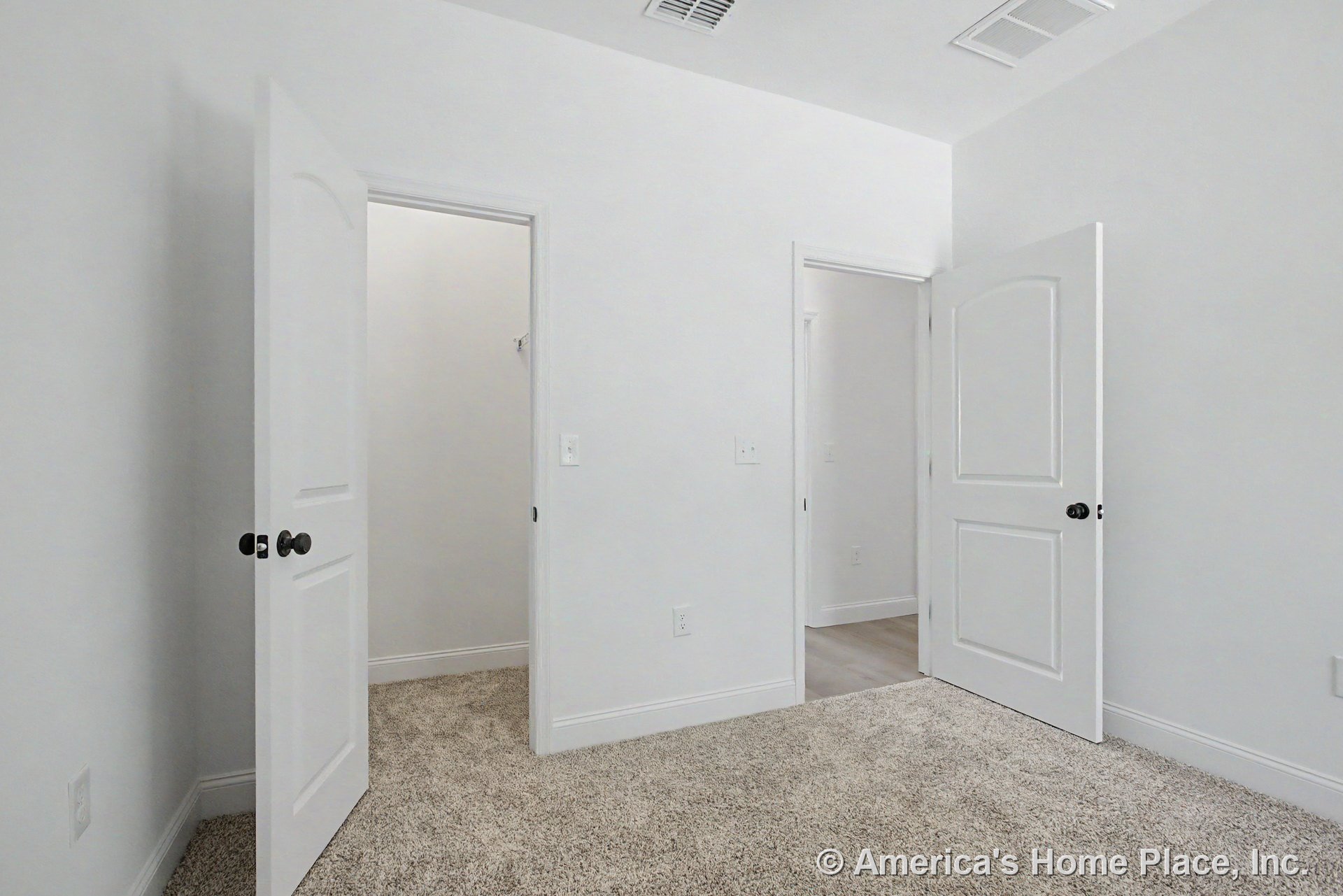 Bedroom with light carpet flooring, two white paneled doors, white painted walls, baseboard trim, closet entry, and ceiling vent.