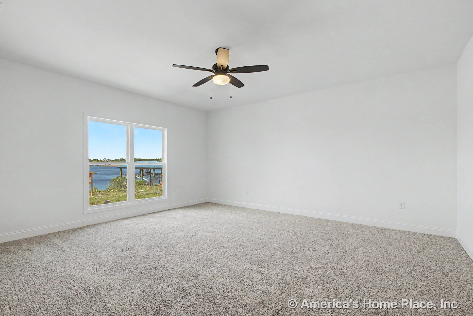 Bedroom with large window overlooking lake, neutral carpet flooring, white walls, simple baseboard trim, ceiling fan with integrated light, and abundant natural light.