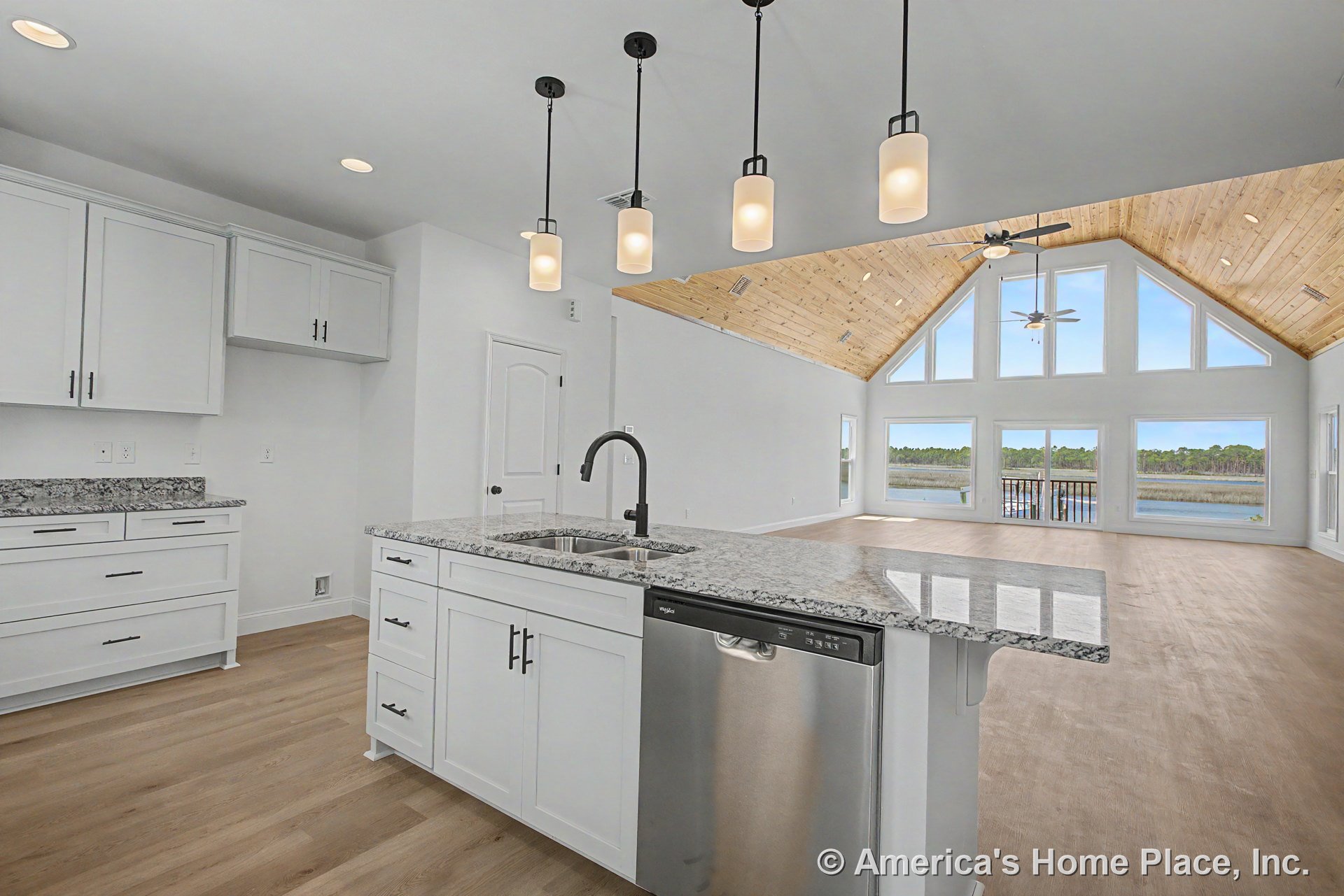Open kitchen with white shaker cabinets, granite countertops, pendant lighting, stainless steel dishwasher, and built-in sink; overlooks living area with vaulted wood ceiling