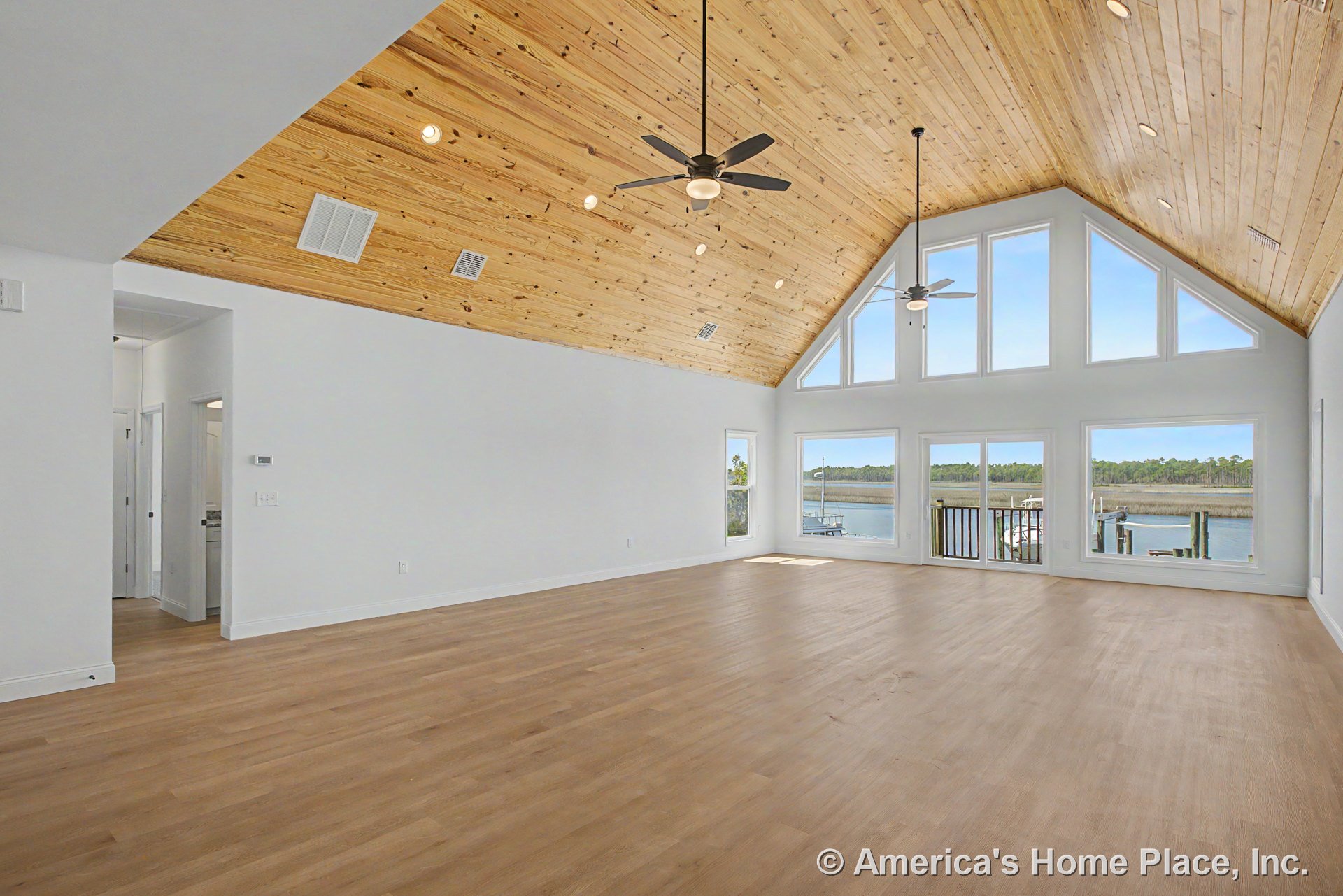Vaulted wood plank ceiling with ceiling fans and recessed lighting, expansive picture windows and glass balcony door framed by white trim, light wood flooring throughout open great
