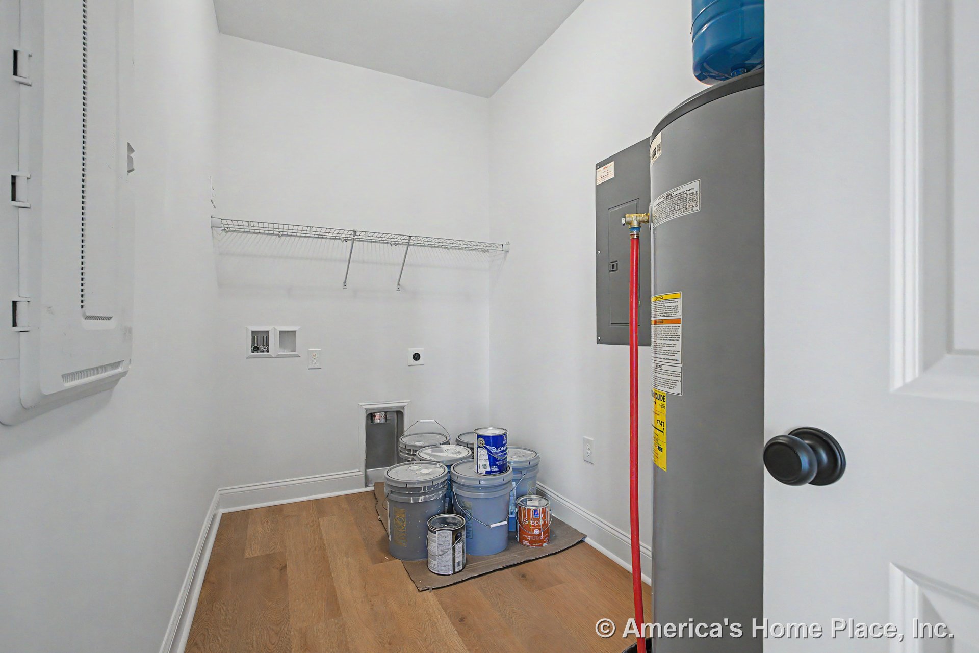 Laundry room with water heater, electrical panel, washer and dryer hookups, wire shelving, white walls, wood-look flooring, and white baseboard trim.