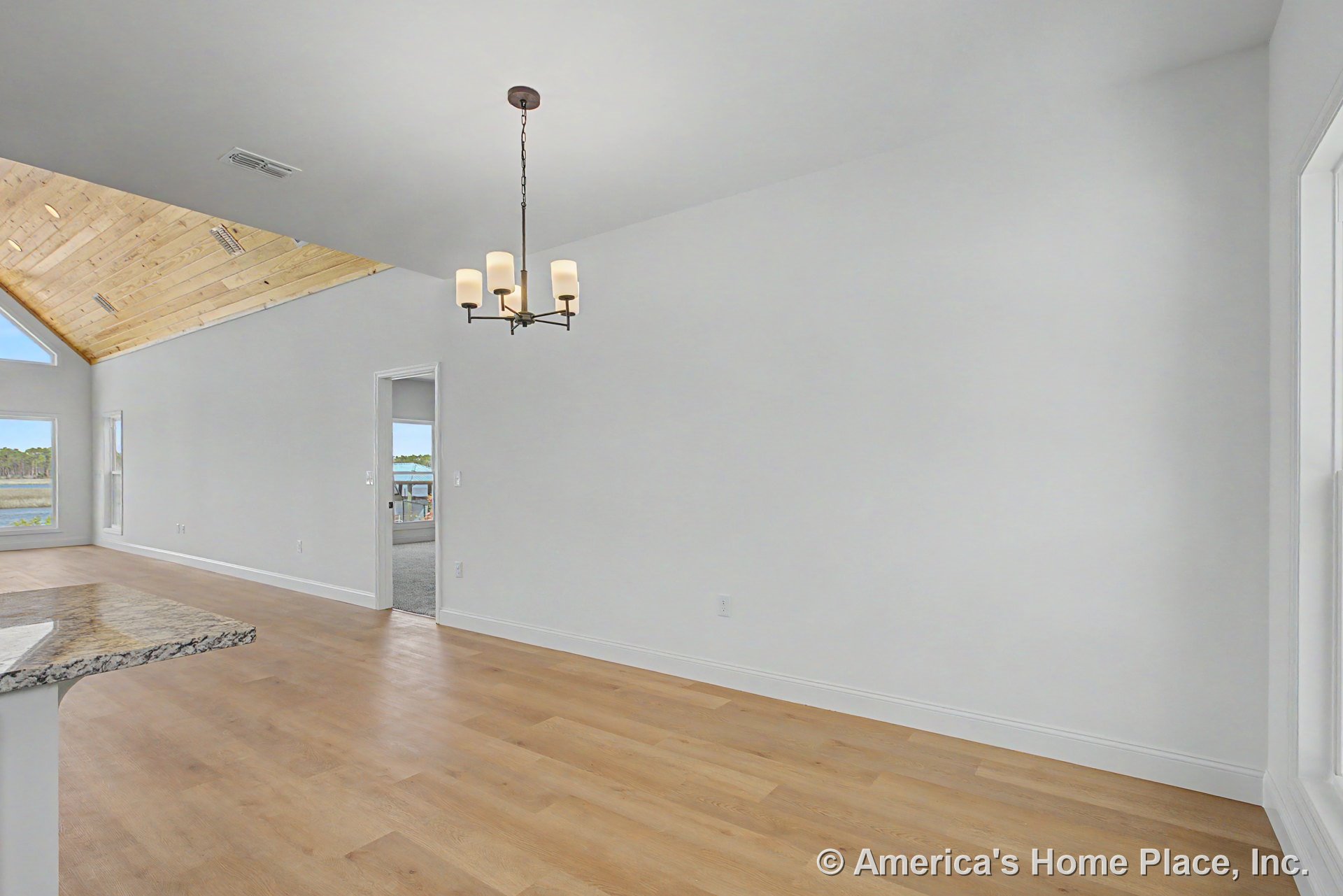 Open dining area with modern chandelier, light wood plank flooring, white walls with baseboard trim, large window, doorway to adjacent room with vaulted wood ceiling, and partial