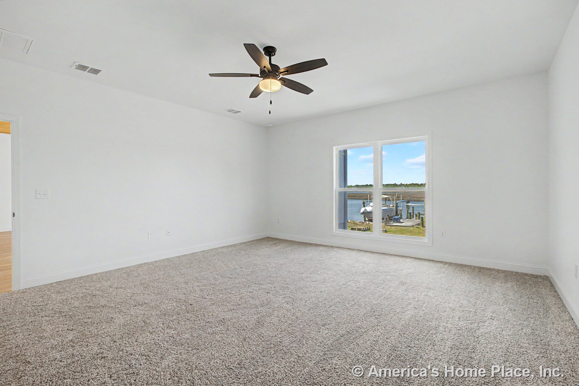 Carpeted bedroom with large double window overlooking waterfront, white walls, ceiling fan with integrated light, baseboard trim, and door.
