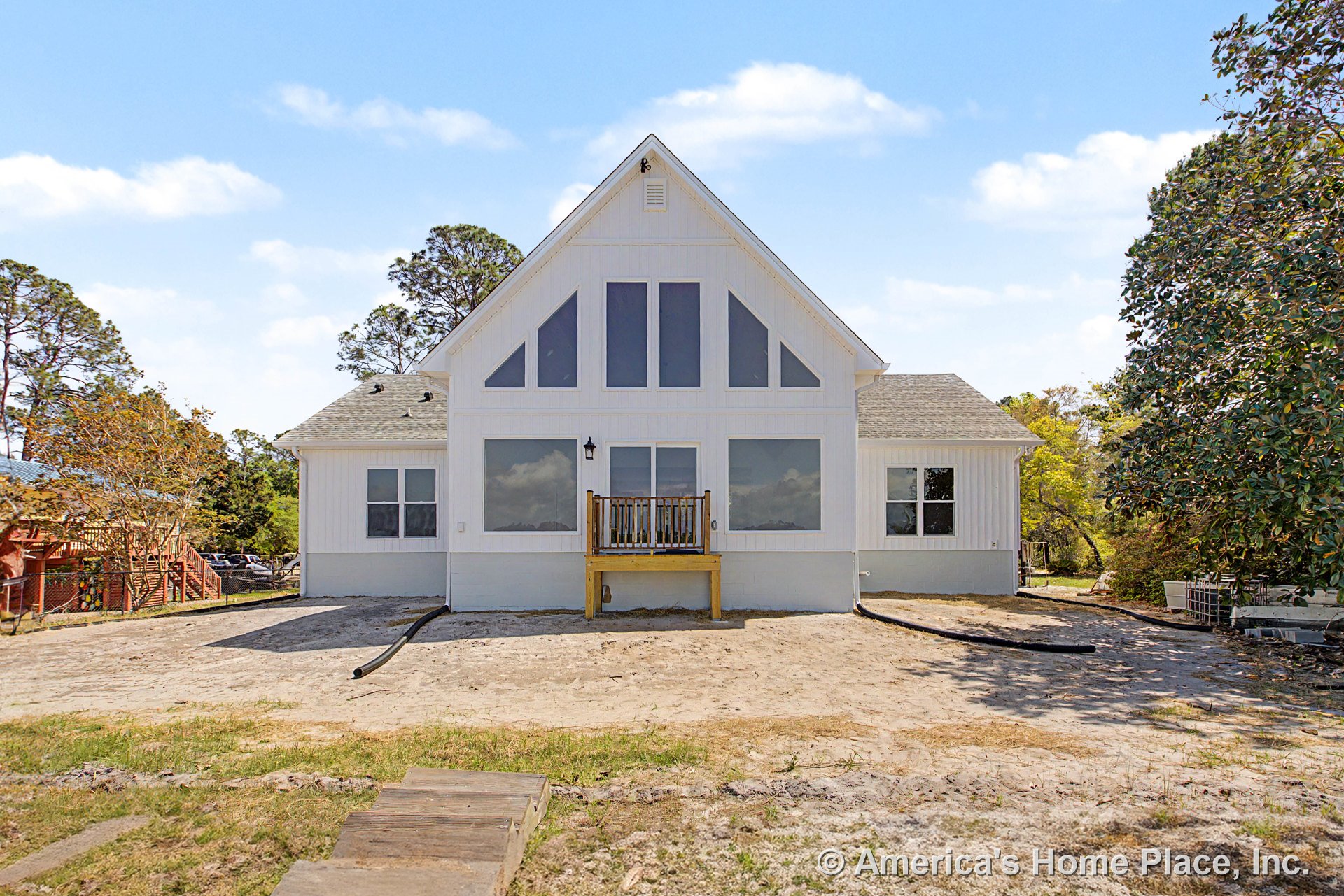 White vertical siding and triangular gable roof with multiple large vertical windows on rear elevation, small elevated porch with wood railing, outdoor wall lantern, and concrete