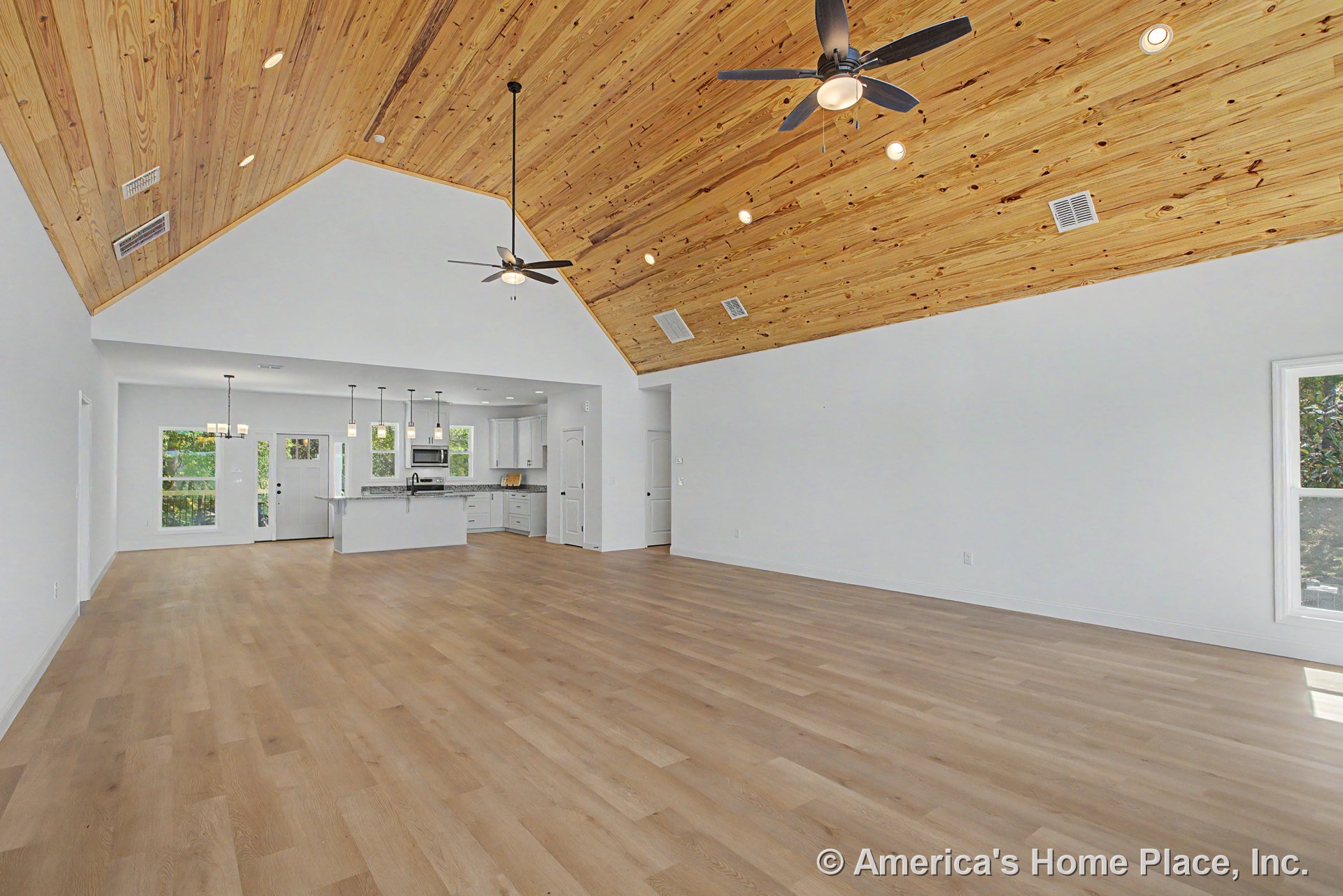 Vaulted wood plank ceiling with recessed lighting above open living area, light hardwood floors throughout, modern kitchen featuring white cabinetry, granite countertops, and