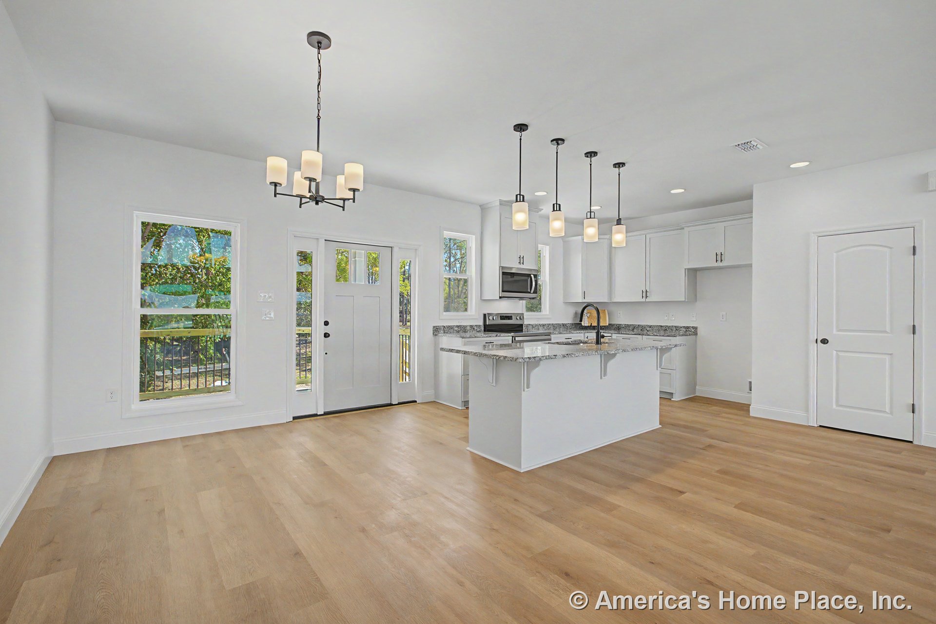 Open kitchen with white shaker cabinets, granite island, multiple pendant lights, light wood flooring, stainless appliances, recessed lighting, large windows, and front entry door