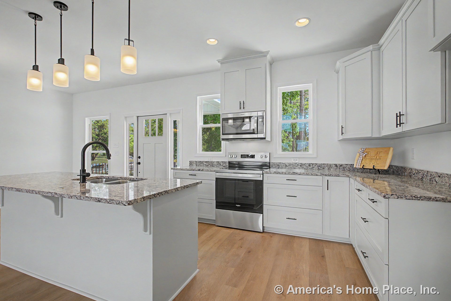 White shaker cabinets and granite countertops in a kitchen with stainless steel range and built-in microwave, pendant lighting above a granite island with undermount sink, wood