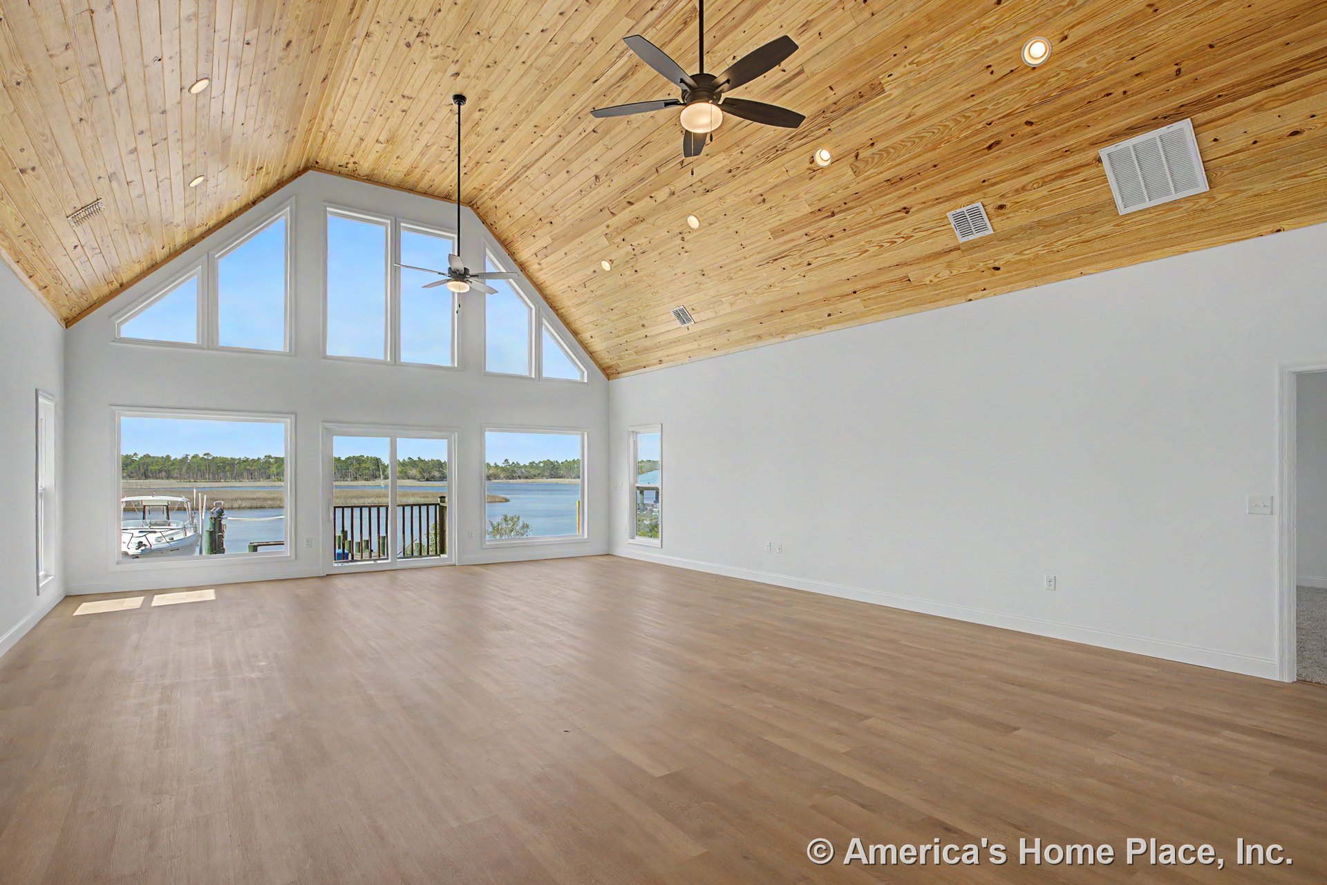 Vaulted wood plank ceiling with recessed lights and ceiling fans, triangular window wall and sliding glass doors framing waterfront view, light wood flooring, white walls, and