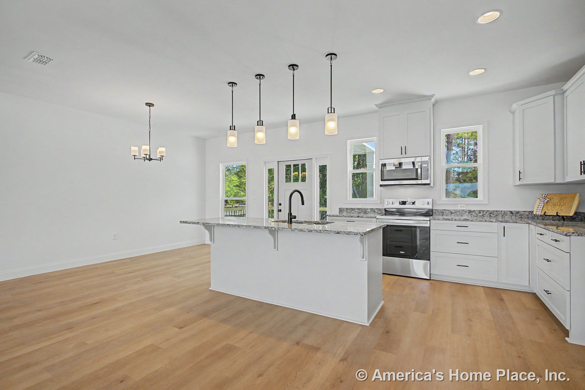 White shaker cabinets and granite kitchen island with stainless steel oven and microwave, pendant lighting above island, light wood flooring, multiple windows, and glass door