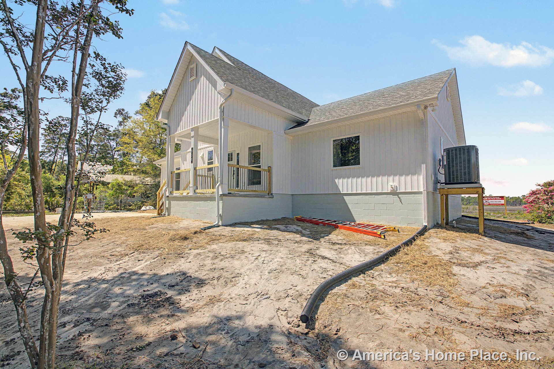 White vertical board siding with multiple windows, covered front porch featuring wood railings and columns, raised concrete foundation with steps, roof-mounted HVAC unit, and