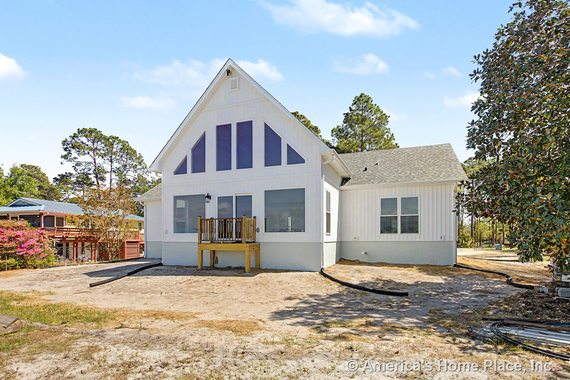 White vertical board and batten siding with a prominent gable roof, large triangular windows, double window units, small elevated porch, exterior wall light fixture, and crisp trim