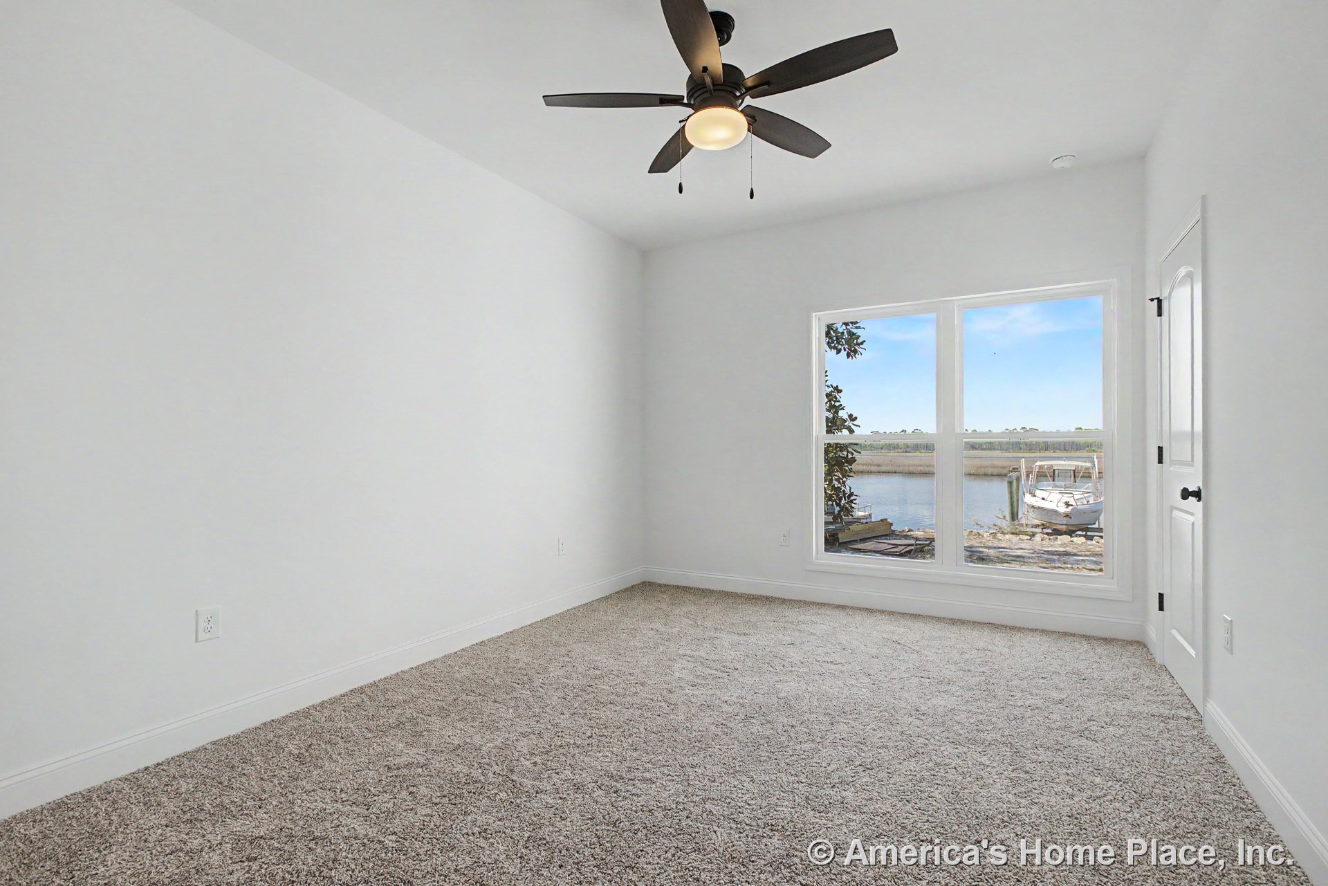 Large bedroom with neutral carpet flooring, white painted walls, large window offering waterfront views, ceiling fan with integrated light fixture, white trim and baseboards, and