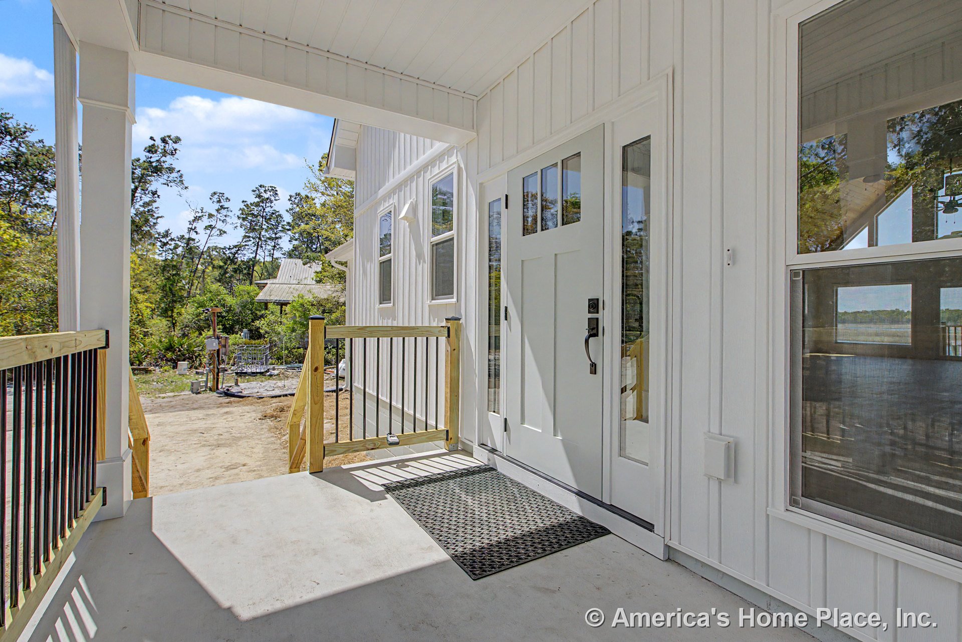 Covered front porch with white board and batten siding, modern entry door with glass sidelights, concrete flooring, wood and metal railing, exterior window trim, and contemporary