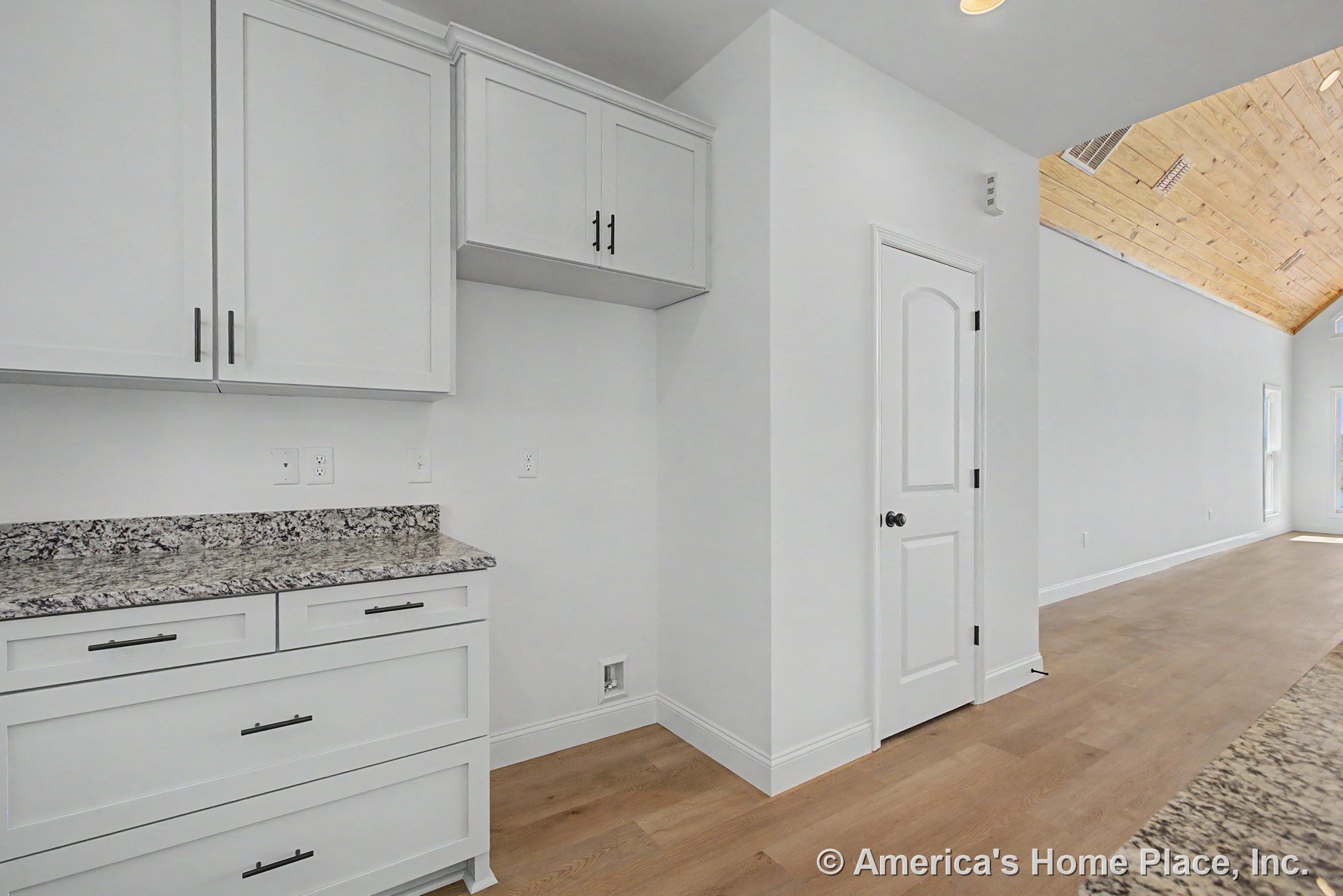 White shaker upper cabinets and drawers, granite countertops, light wood flooring, vaulted wood ceiling with recessed lighting, white interior door and trim.