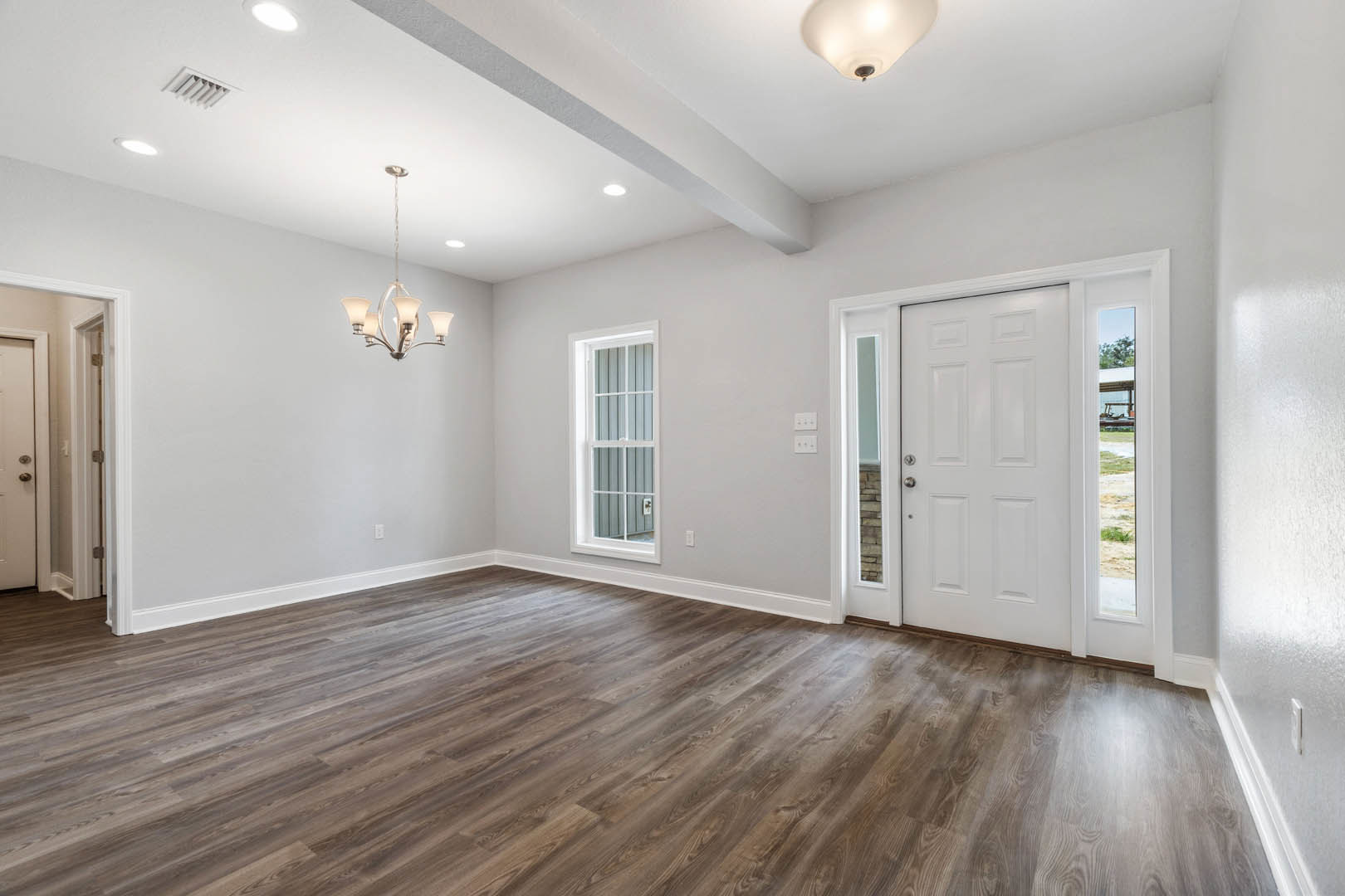 Wood flooring in a room with white walls, a paneled door, and a modern chandelier hanging from the ceiling