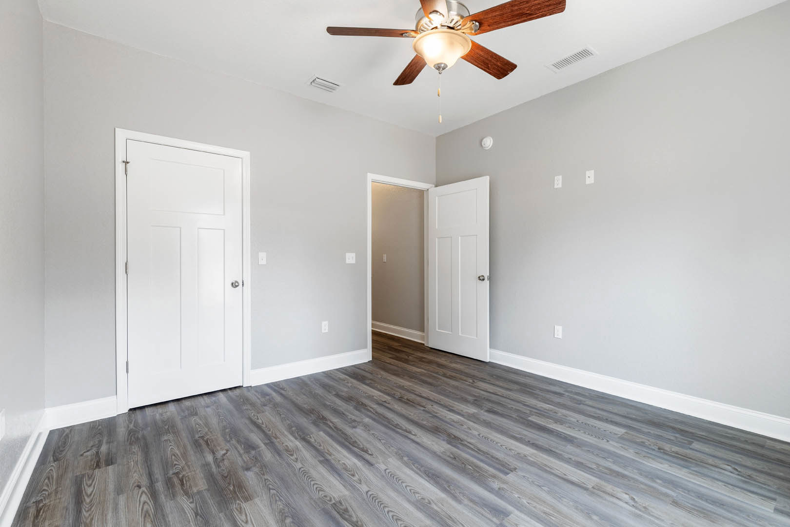 Ceiling fan with light fixture, white doors with silver knobs, wood laminate flooring, white walls with light switch