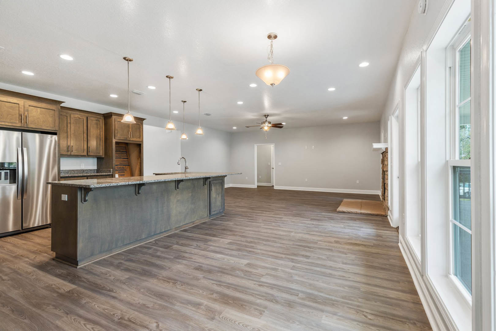 Open kitchen and dining area featuring wood floors, marble countertop, stainless steel refrigerator, white cabinetry, modern light fixture, and a white door with silver handle.