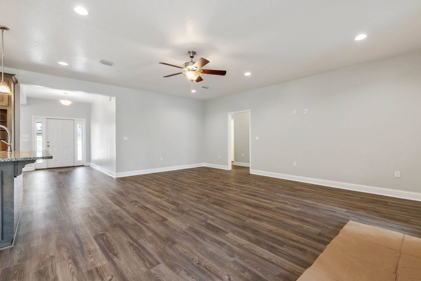 Ceiling fan with light fixture, hardwood flooring, white walls, glass-paneled door, and a piece of paper on the floor