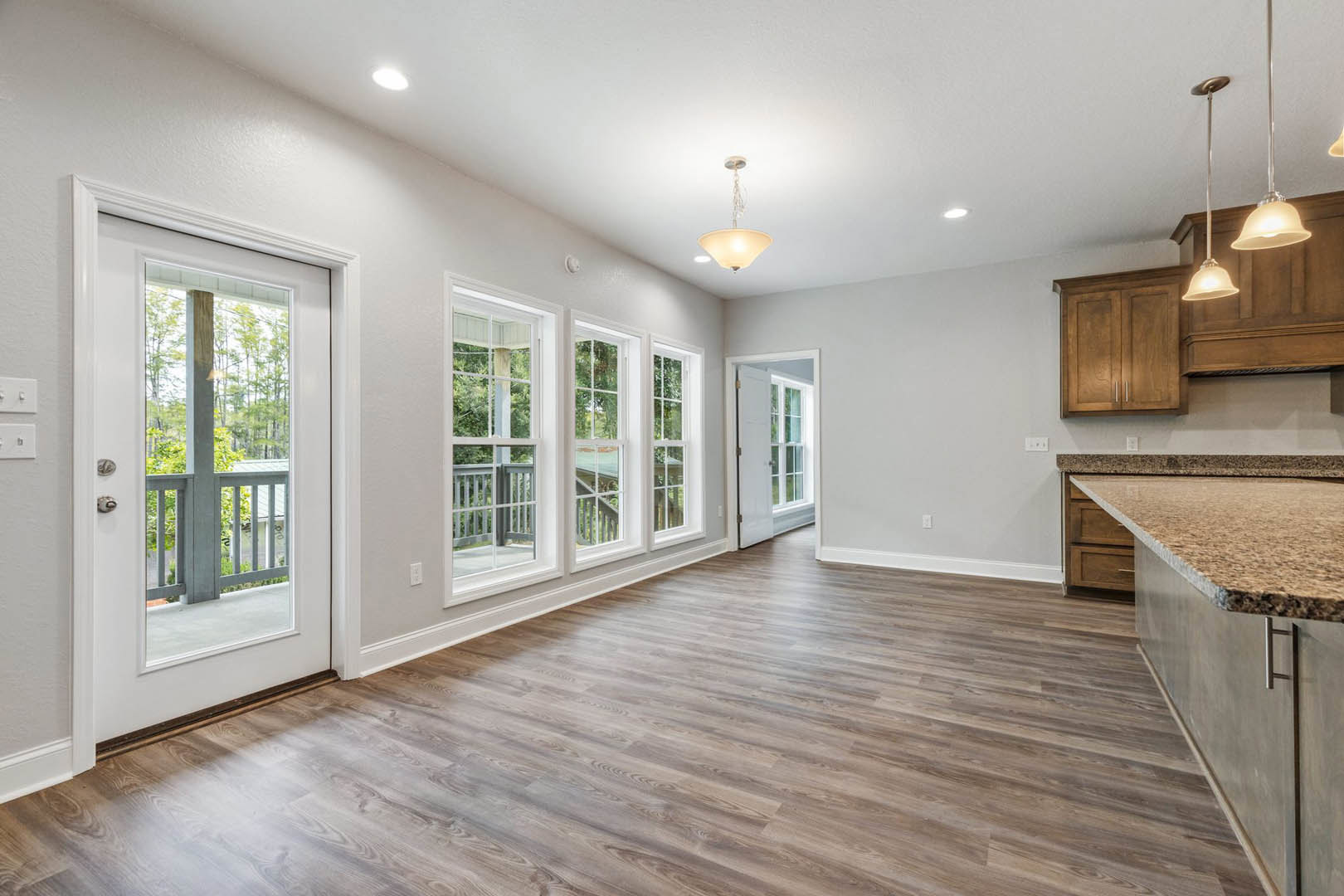 Open kitchen with hardwood flooring, white cabinetry, stone countertop, glass door leading to balcony with metal railing, recessed lighting, and large windows.