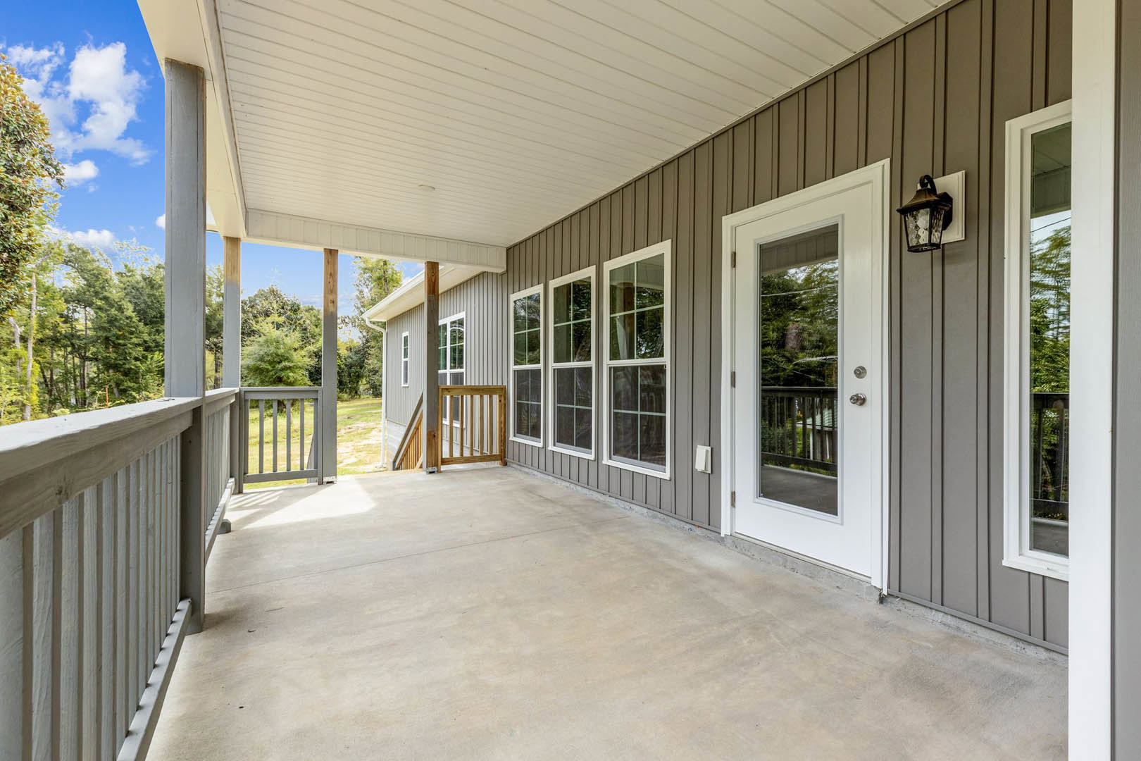 White porch with wooden railing, glass-paneled white door, window with white frame, and black metal light fixture