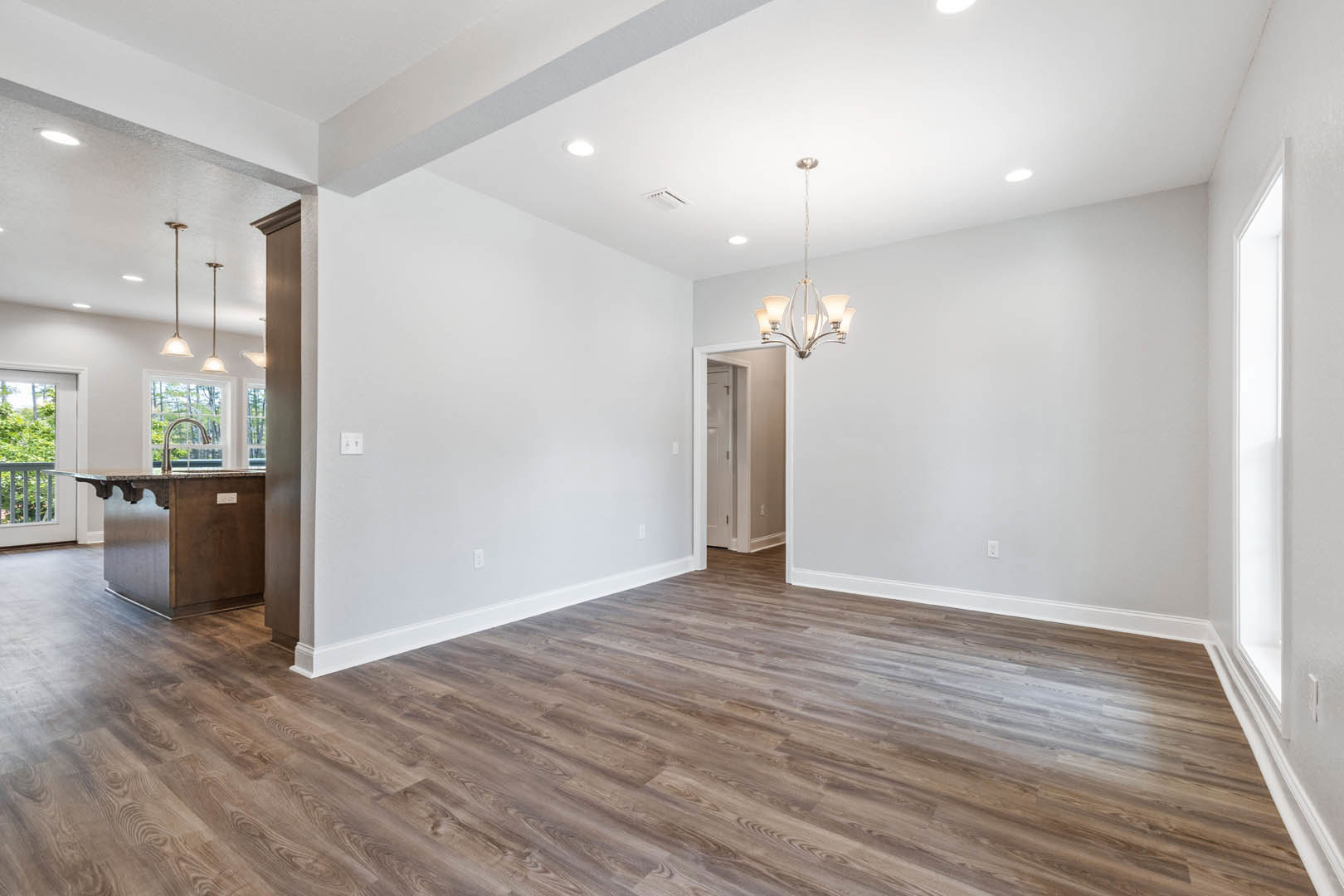Hardwood floor room with chandelier, marble kitchen island, ceiling vent, and balcony view of trees