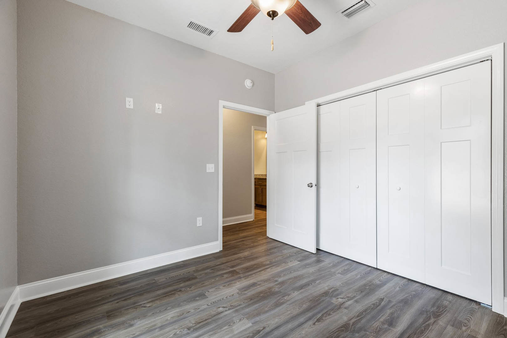 Room with wood laminate flooring, white paneled doors, ceiling fan with light fixture, and silver door knob against plaster walls