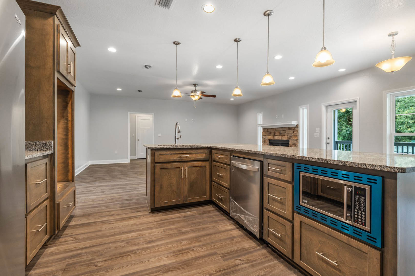 Spacious kitchen featuring a large central island with white countertop, wood flooring, stainless steel refrigerator, blue microwave with glass door, white appliance with black