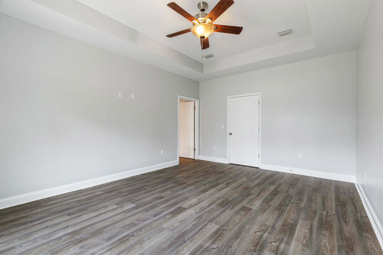 Ceiling fan with light fixture, hardwood floor, white walls, white door with silver knob and decorative cross