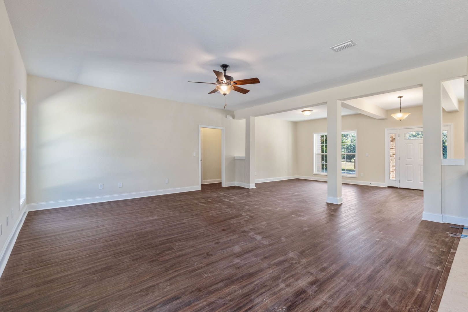 Spacious room with hardwood floors, white walls, ceiling fan with light, white door, and rectangular wall trim