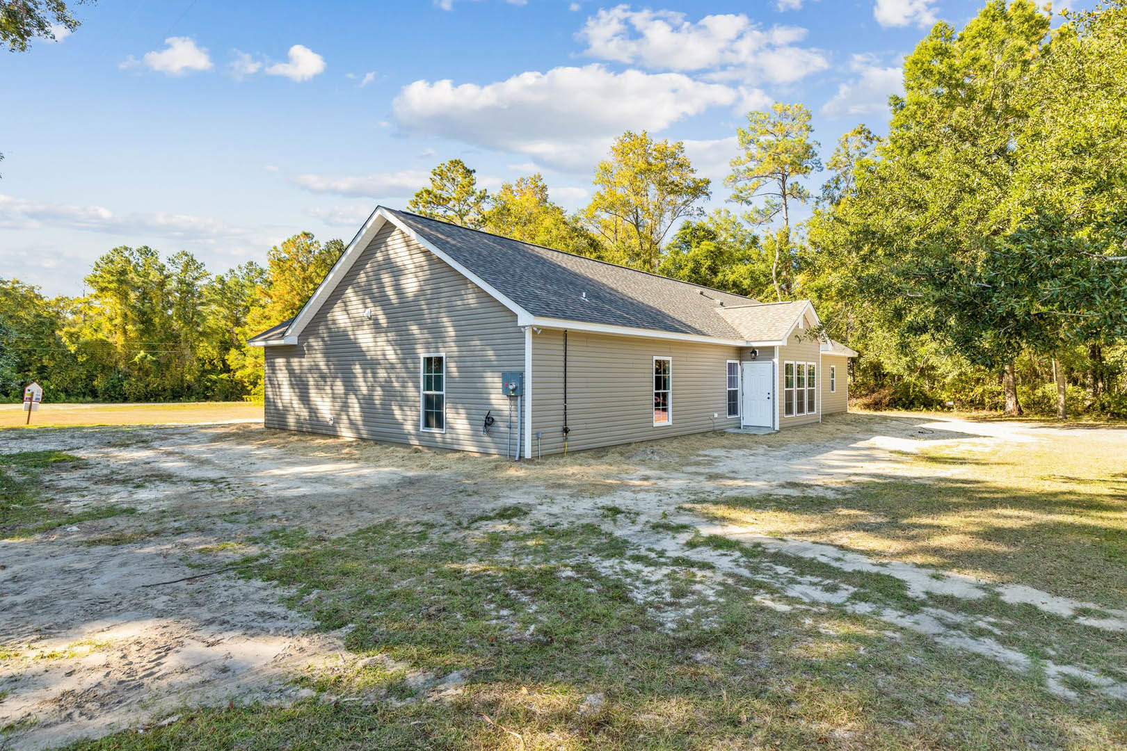 Two-story cottage with white trim, black door hardware, grassy front yard, mature leafy trees, and partly cloudy sky in the background