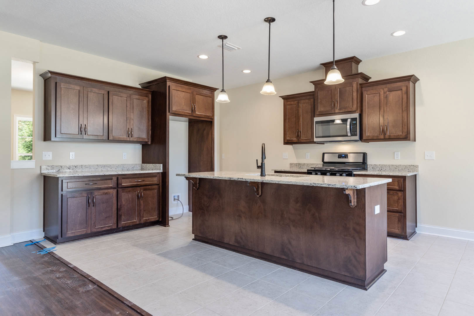 Spacious kitchen featuring a marble-topped island, stainless steel stove, white cabinetry, built-in microwave, and light wood flooring