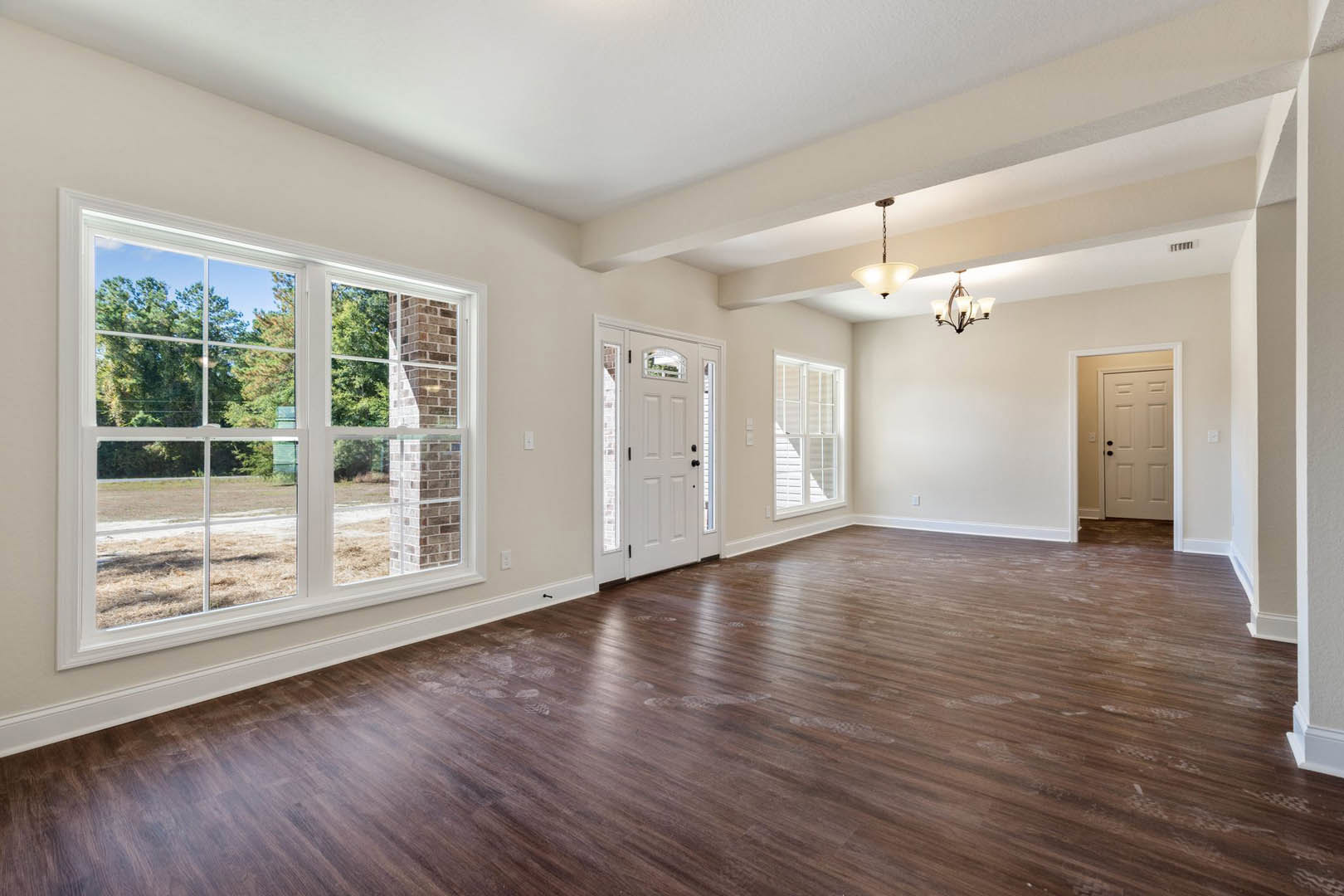 Hardwood floor with visible footprints, white ceiling, white door with glass panes and black knobs, window showing brick chimney and trees outside