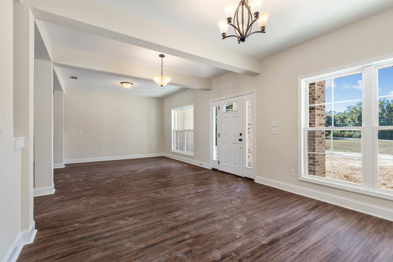 Wood floor room with white doors, chandelier, window framed by brick column, and view of trees outside