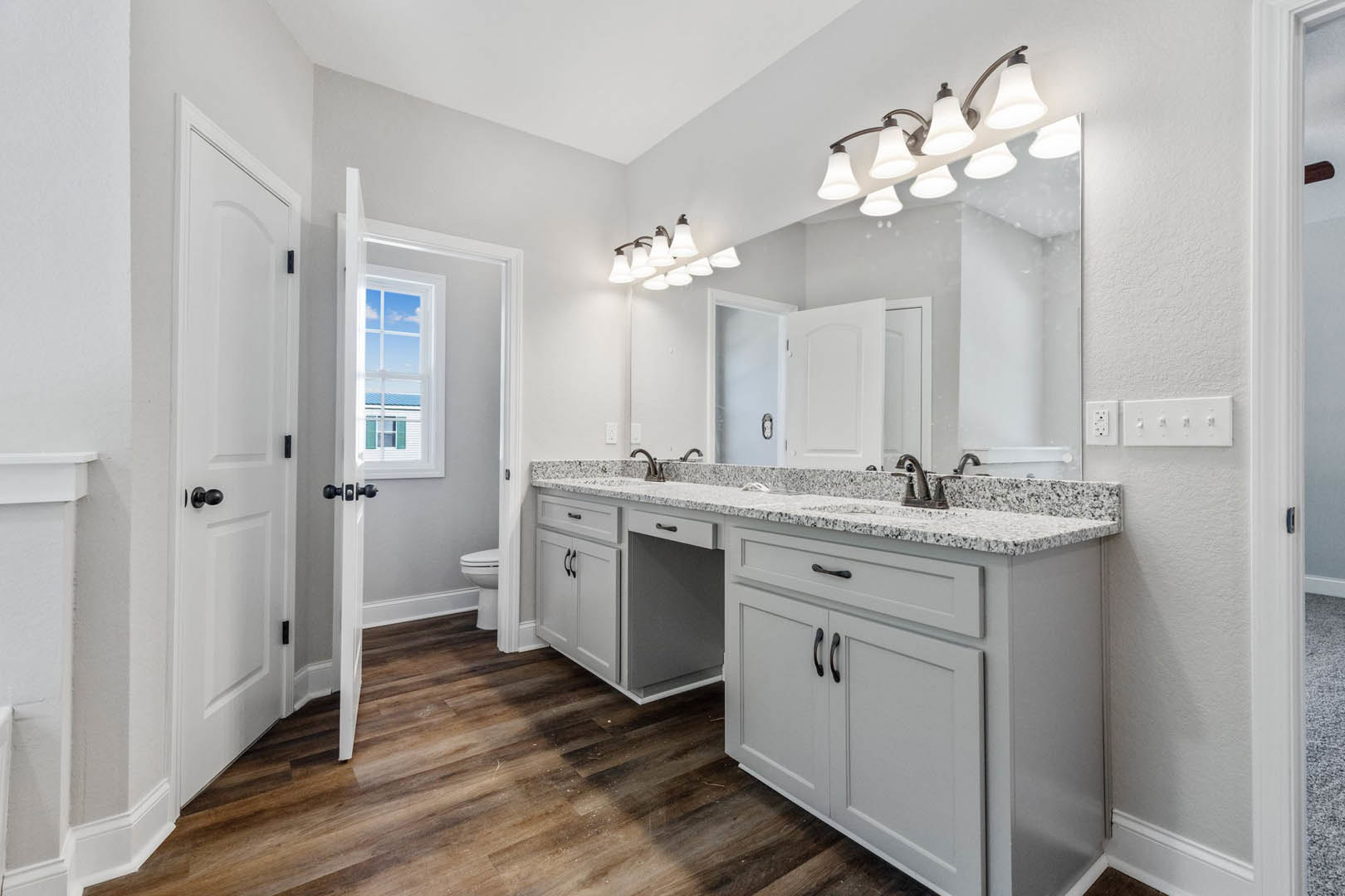 Bathroom featuring a wide marble countertop, expansive mirror above, row of modern light fixtures, wood flooring with visible white mold, white door with black knob and window