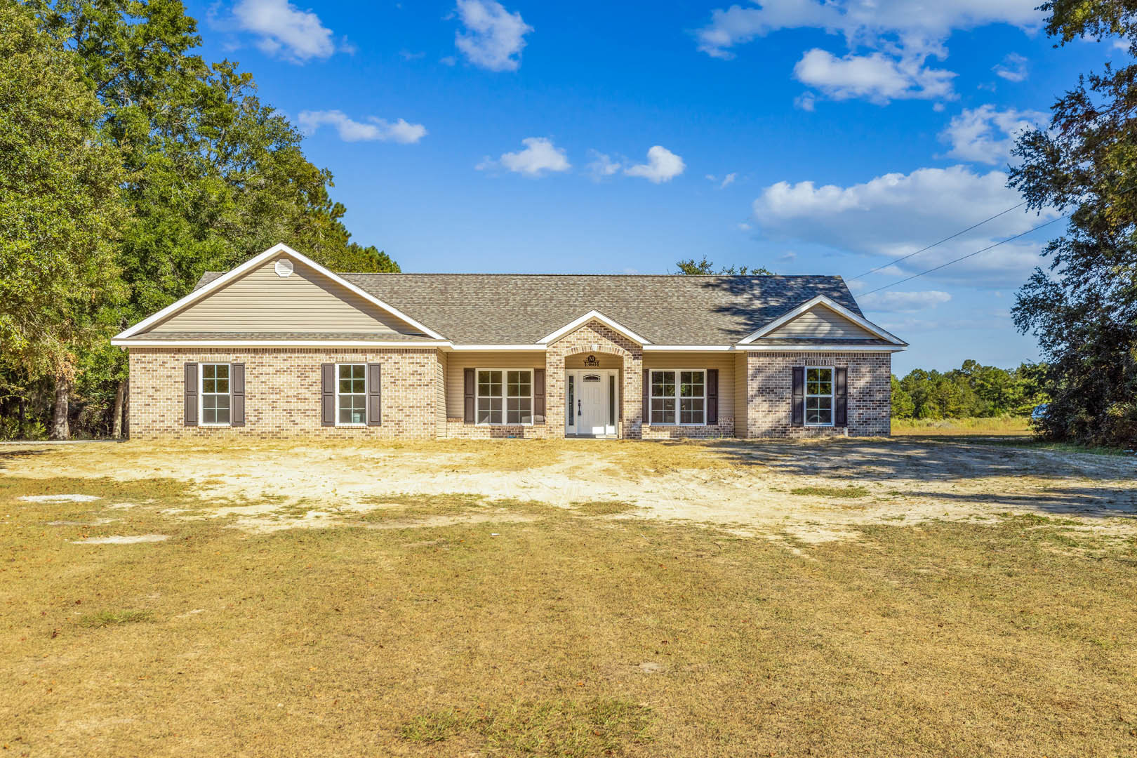 Two-story house with white doors and multi-pane windows, surrounded by a dirt and patchy grass yard under a cloudy sky.
