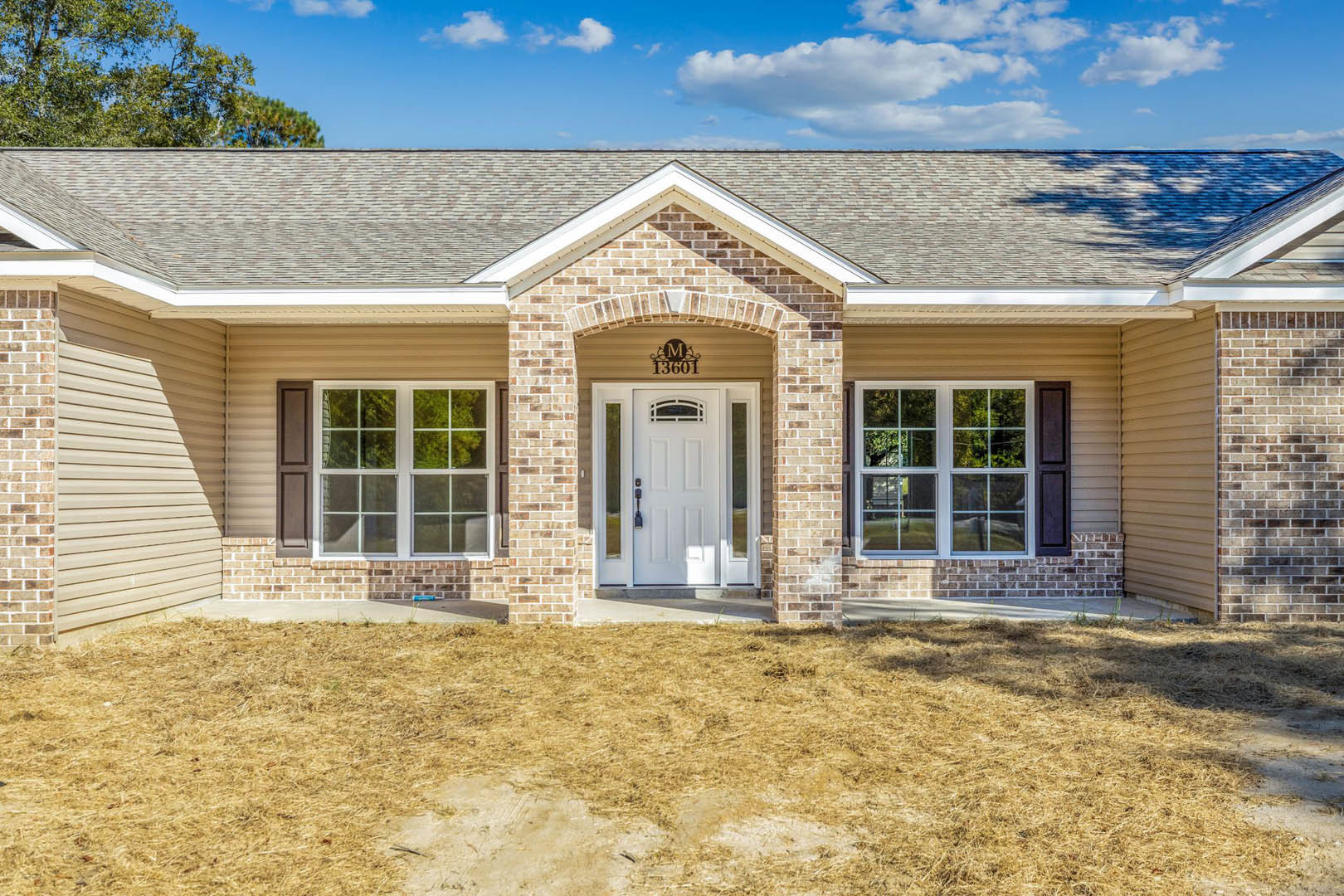 Red brick exterior with white framed windows and a white front door featuring glass panes, small grassy yard in front, cloudy sky overhead