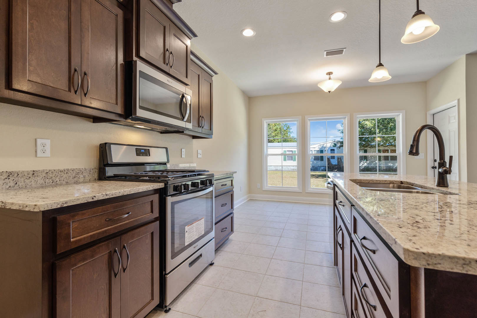 Granite countertops, white cabinetry, stainless steel stove and oven, built-in microwave, modern light fixture, electrical outlet, undermount sink