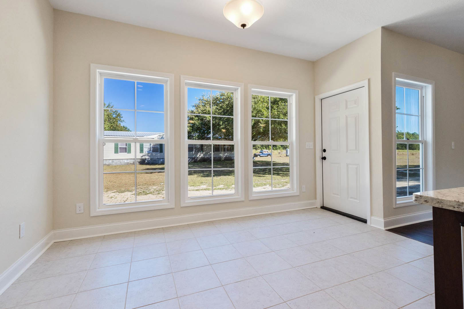 White tile floor and white walls, white door with black knobs, row of windows showing trees and neighboring house, close-up of modern light fixture.