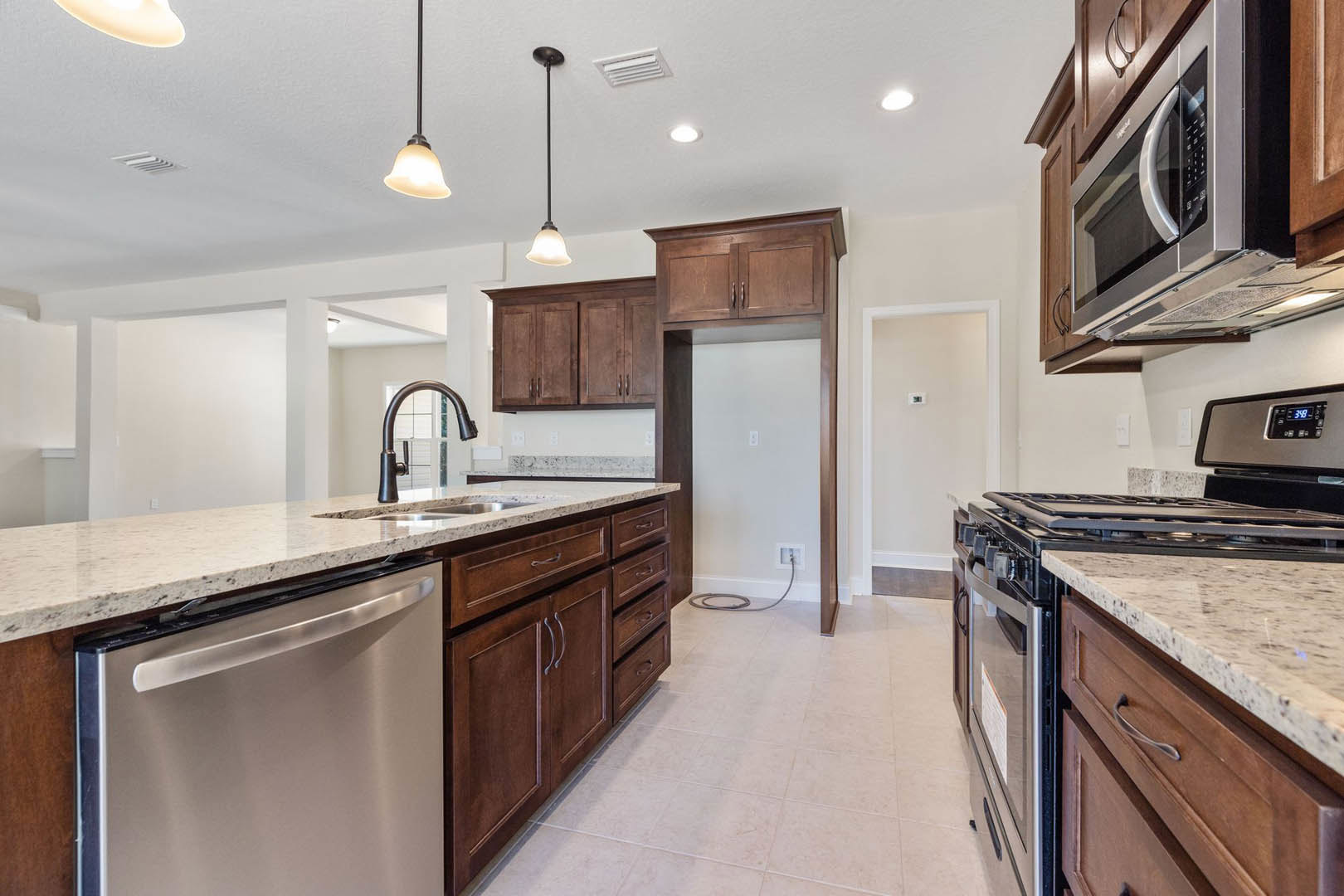 White kitchen with shaker cabinets, stainless steel stove and oven, built-in microwave, undermount sink with chrome faucet, light stone countertops, and integrated dishwasher