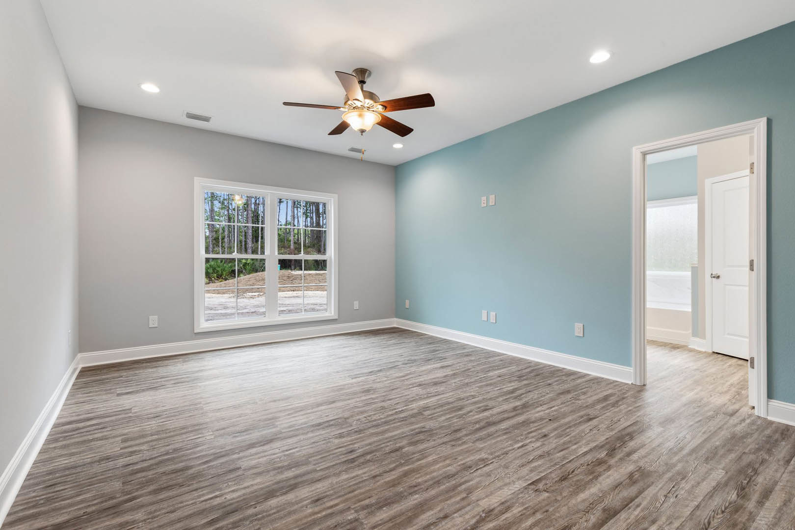 Ceiling fan with light fixture, wood flooring, white walls, window showing trees outside, white door with silver handle