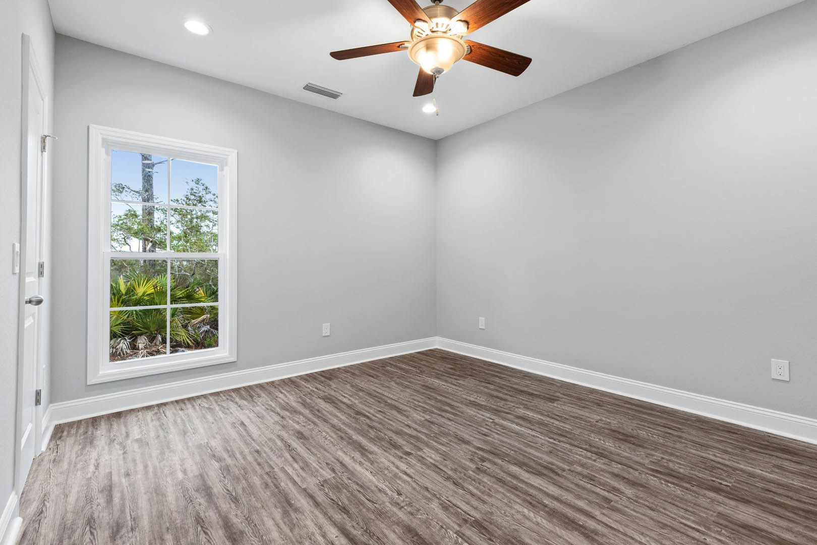 Wood flooring and plaster walls in a room with a ceiling fan and light fixture, large window overlooking trees, small potted plants on the sill