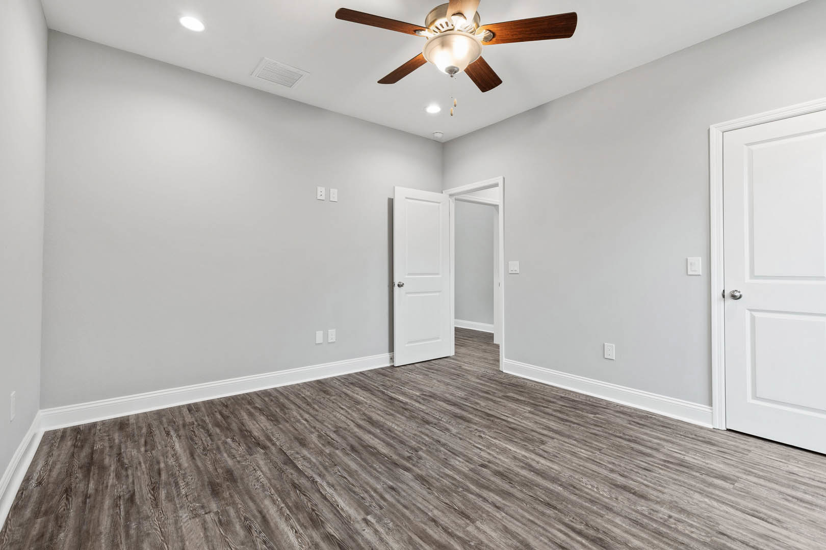 Bedroom with wood laminate flooring, white paneled door with silver knob, plaster walls, and ceiling fan with integrated light fixture