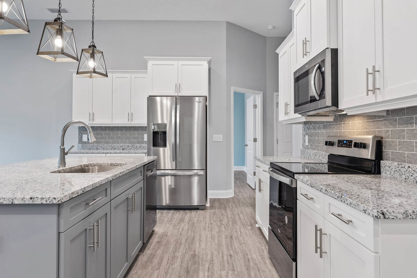 Granite countertops, stainless steel refrigerator with water dispenser, built-in microwave with handle, metal-framed pendant light, close-up of stove and faucet, white cabinetry