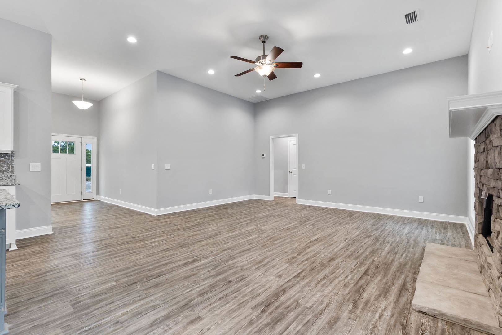 Spacious room with wood flooring, ceiling fan with light fixture, stone slab on floor, white door with window, plaster walls, and black square accent with linear design