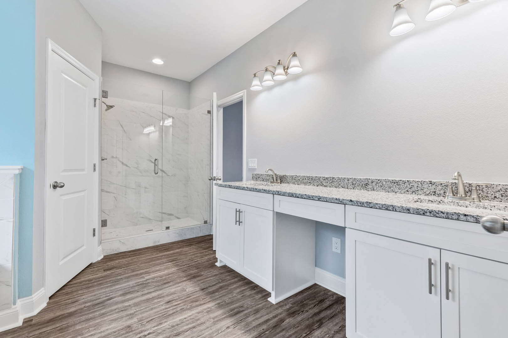 Bathroom featuring marble countertops, glass shower enclosure, wood flooring, white cabinetry, four-light fixture, and chrome faucet.