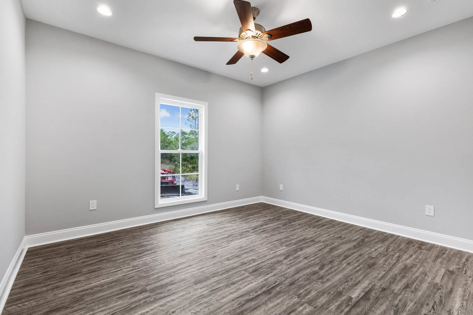 Ceiling fan with light fixture, large window overlooking trees, wood flooring, white walls with crown molding